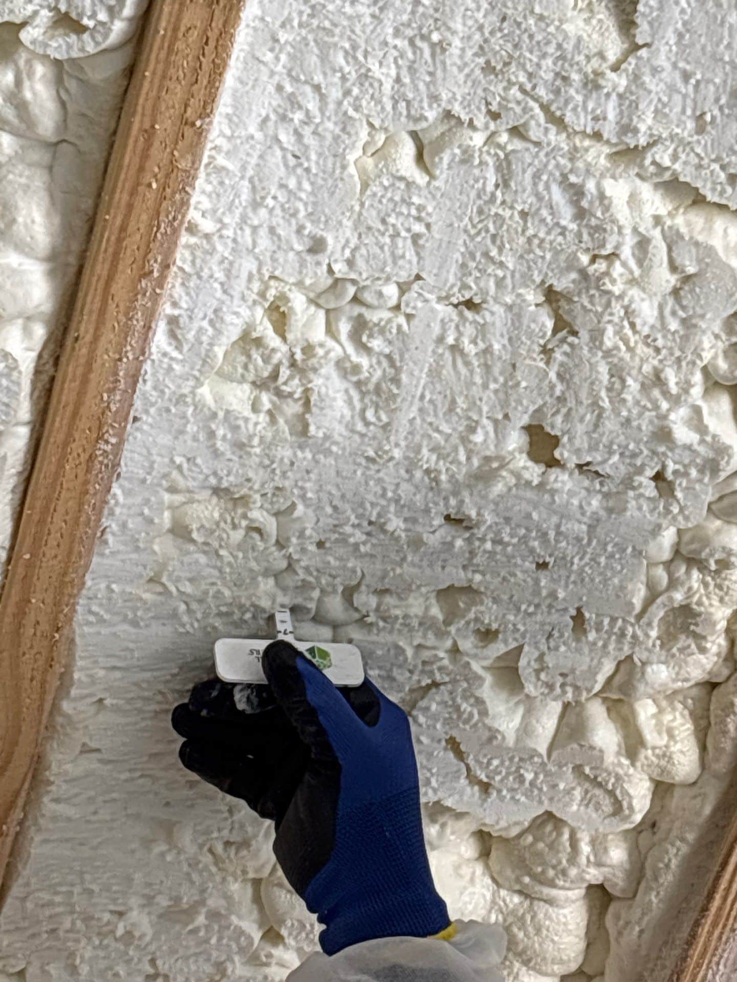 team member testing the thickness of spray foam that has been sprayed onto wall